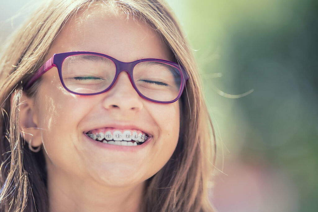 Young girl with glasses and braces smiling outside